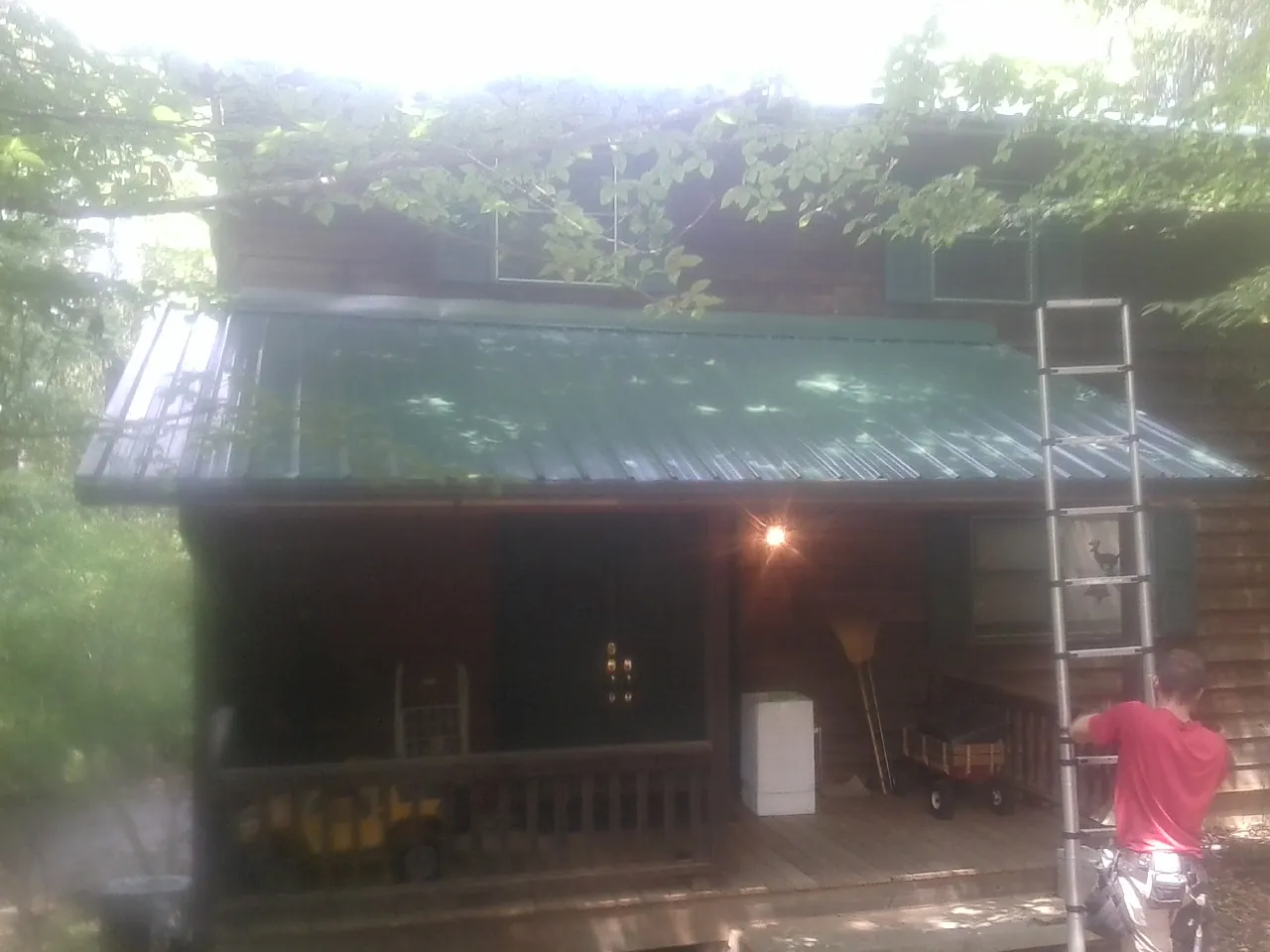 Worker on a ladder at the green porch roof of a wooded cabin in Ingleside